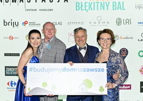Cztery osoby pozują z banerem #budujemydomnazawsze.