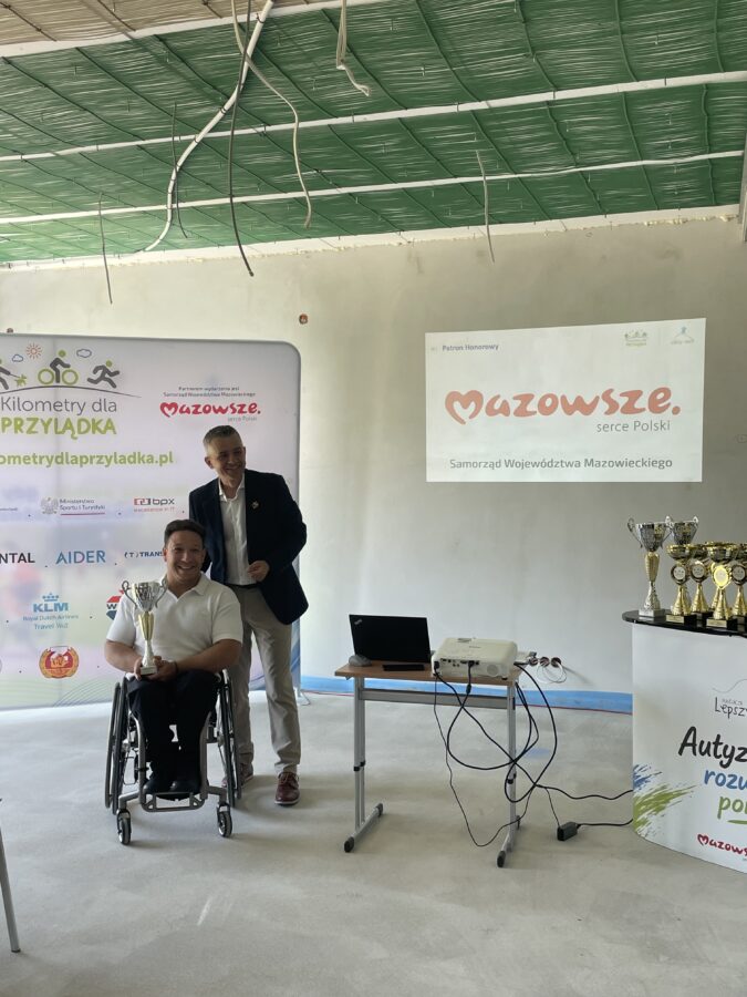 Prezes Fundacji Lepszy Start Łukasz Łań z barierołamaczem Arturem Świerczem na tle ścianki z logo firm i instytucji zaangażowanych w akcję.